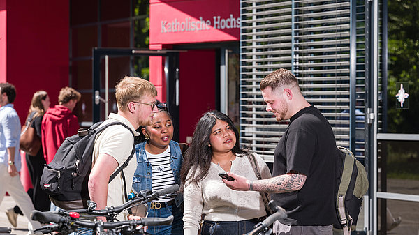 Gruppe von 4 Studierenden steht an den Fahrradständern vor dem Eingang der Hochschule und unterhält sich.