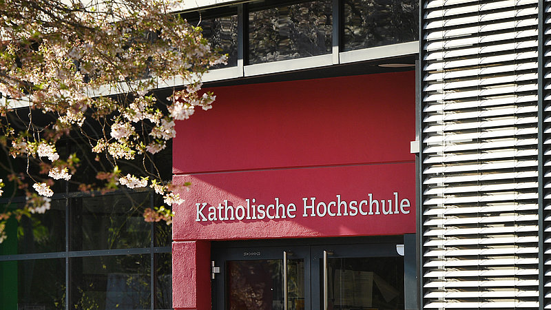 Haupteingang der Katholischen Hochschule Mainz. Im Vordergrund steht ein Kirschbaum.